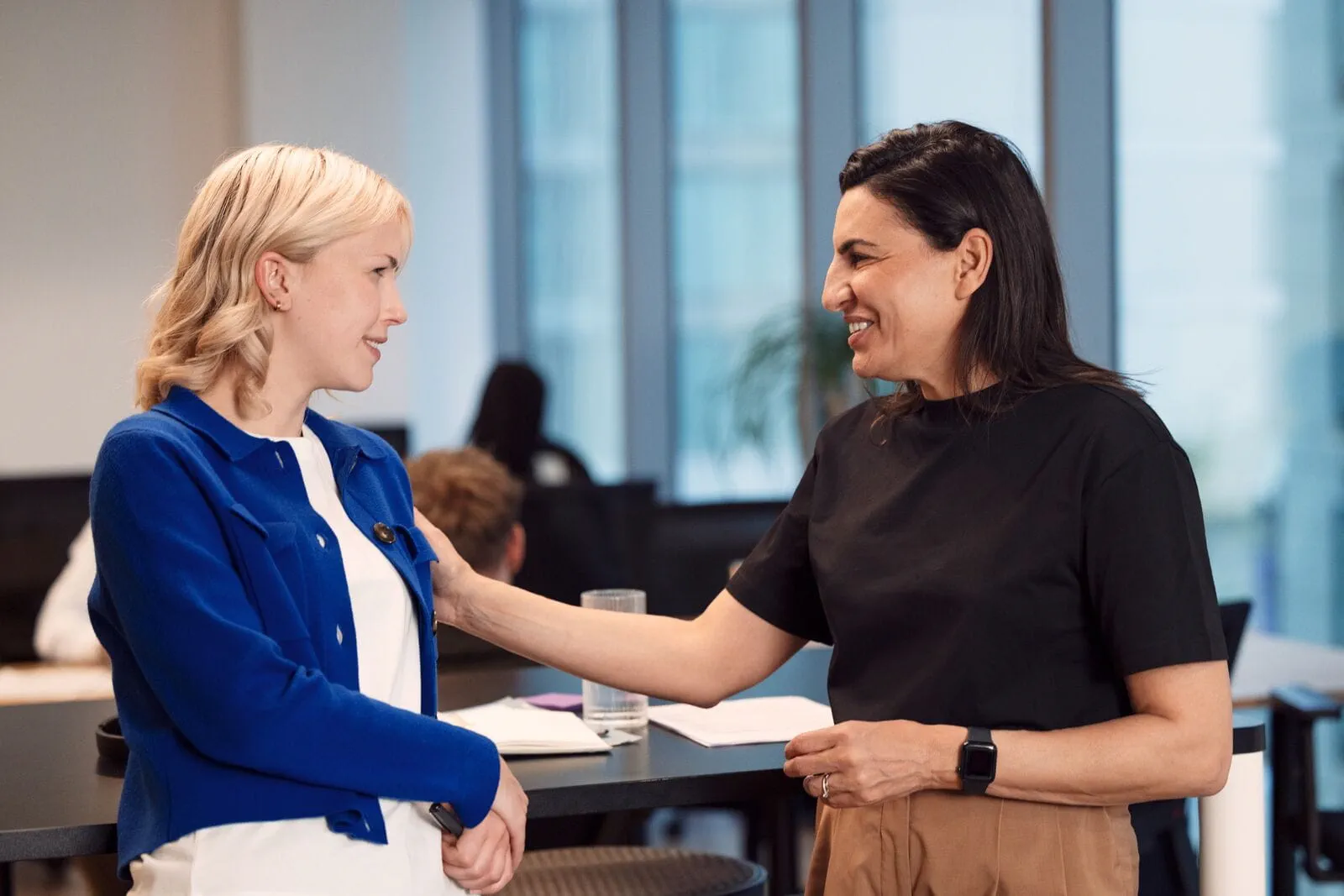 Deux femmes en entreprise souriantes avec geste de soutien, représentant les avantages de l’intérim et l’accompagnement professionnel Deux femmes en entreprise souriantes avec geste de soutien, représentant les avantages de l’intérim et l’accompagnement professionnel