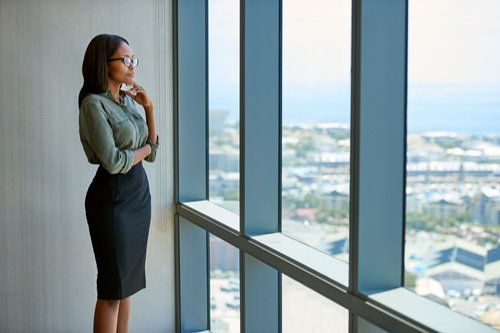 Une jeune femme d'affaires séduisante portant des lunettes regarde pensivement à travers les fenêtres du bureau l'horizon de la ville Une jeune femme d'affaires séduisante portant des lunettes regarde pensivement à travers les fenêtres du bureau l'horizon de la ville