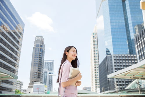 A businesswoman holding a report, with office buildings in the background