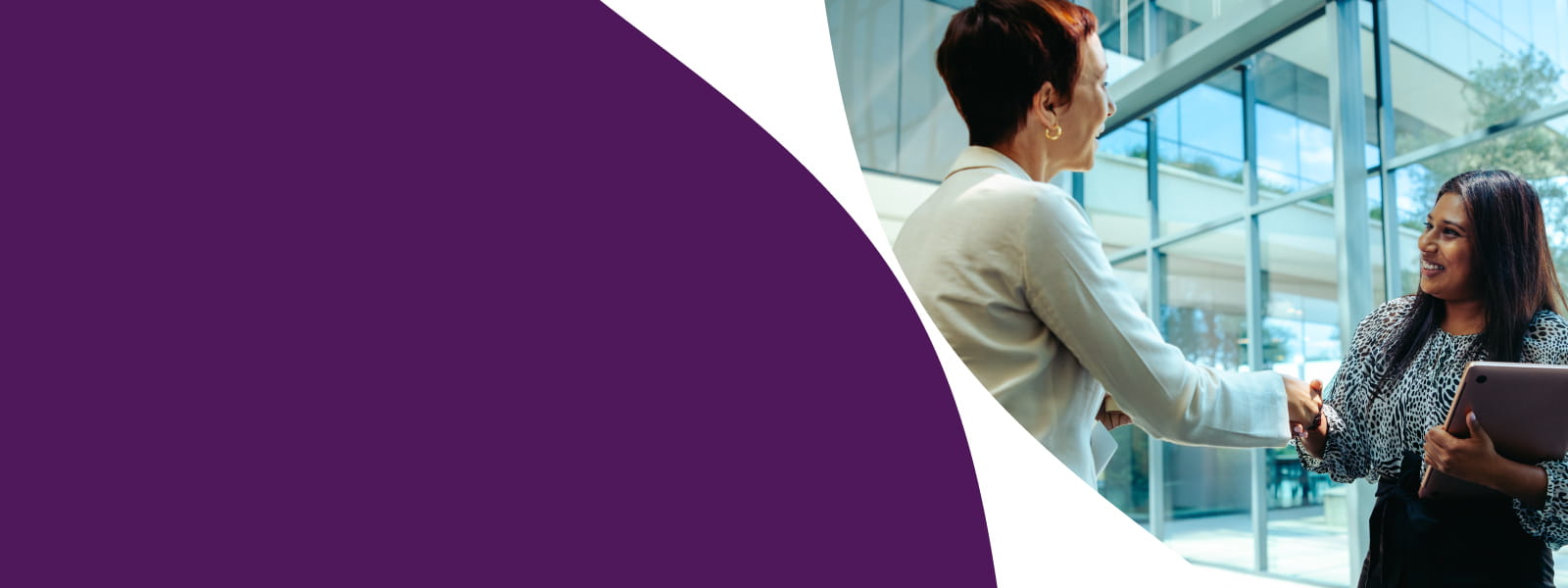 Deux collaboratrices debout se serrant la main et souriant lors d’un échange professionnel.