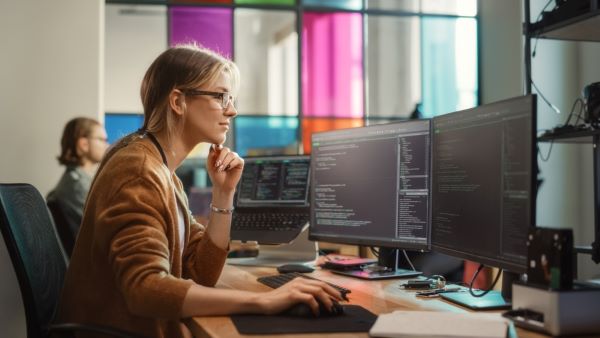 Code d'écriture d'ingénieur logiciel féminin sur un ordinateur de bureau avec plusieurs écrans
