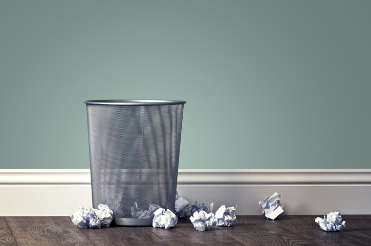trash can surrounded by crumpled pieces paper on the ground
