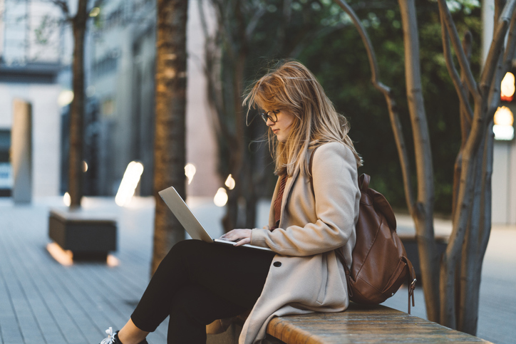 woman sitting on bench with open laptop